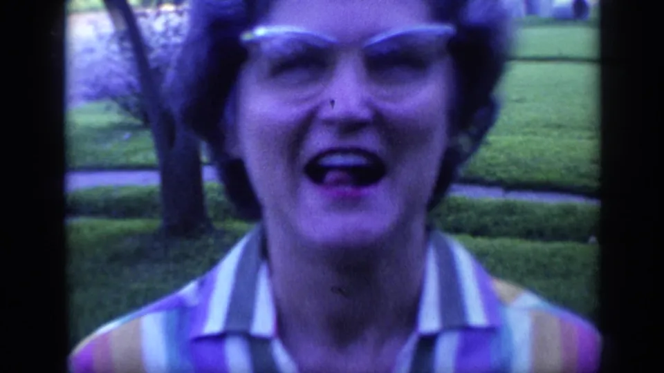 Close 1968 Florida home-movie frame of a woman in glasses making a playful open-mouth expression, with lawn and trees in the background.