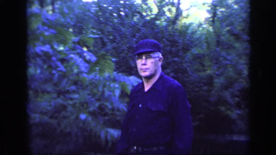 Adult man in a dark cap, glasses, and dark shirt seen in wooded Florida home-movie footage from 1968.