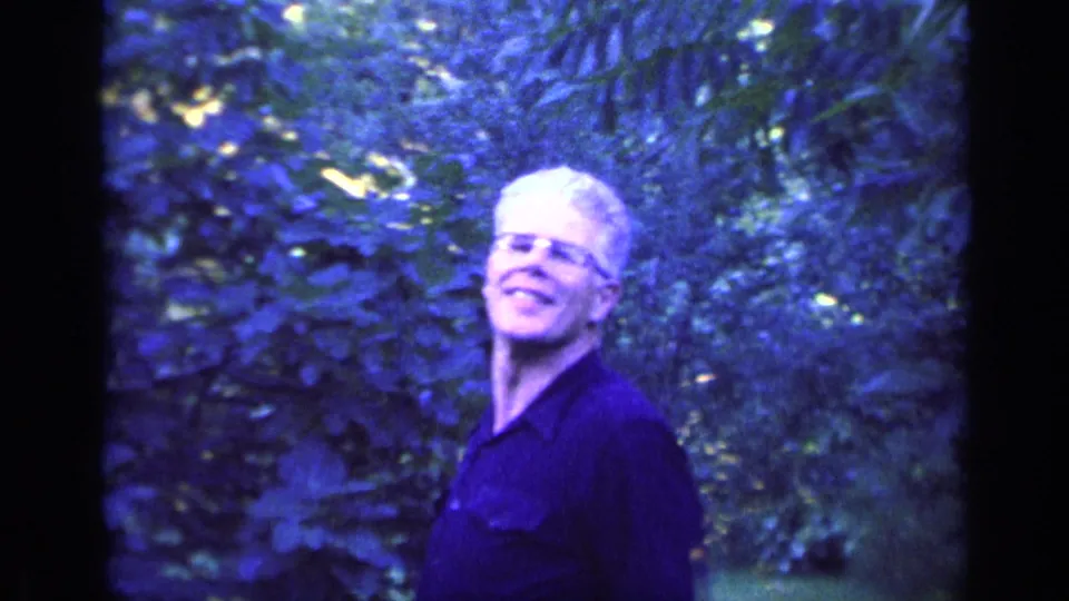 The man smiles toward the camera after removing his cap in the wooded 1968 Florida home-movie scene.