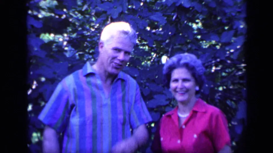 A man in a striped shirt and a woman in a red collared shirt stand together smiling in a Florida backyard scene.