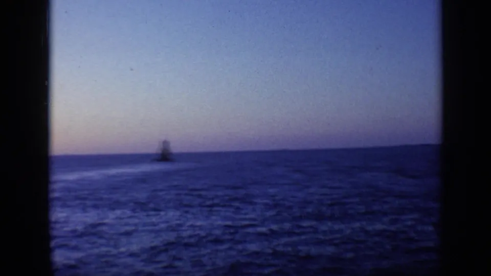 Distant lighthouse or beacon on the Florida horizon over dark blue water, filmed from a boat near dusk in 1968.