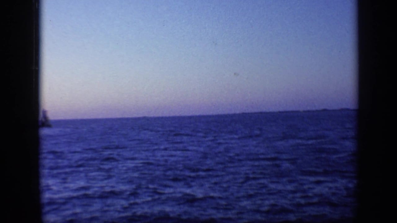 1968 Florida 8mm frame showing blue water, pale dusk sky, distant land, and a small dark shape near the left edge.