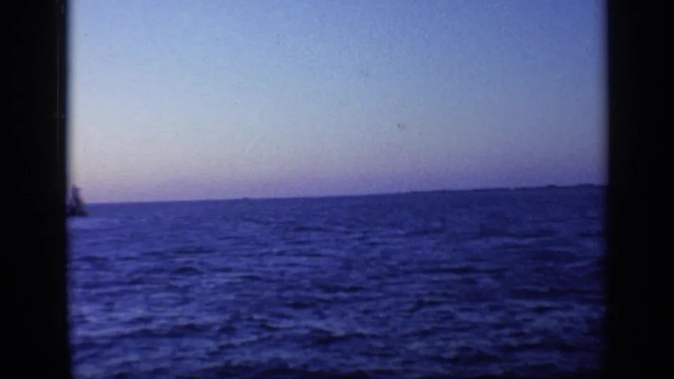 1968 Florida 8mm frame showing blue water, pale dusk sky, distant land, and a small dark shape near the left edge.