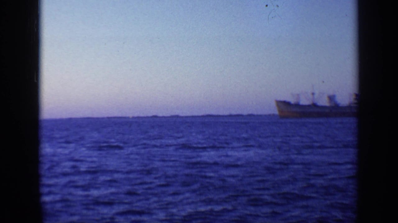 1968 Florida 8mm frame with a distant cargo ship on the right, open water in front, and a faint land horizon under a pale sky.