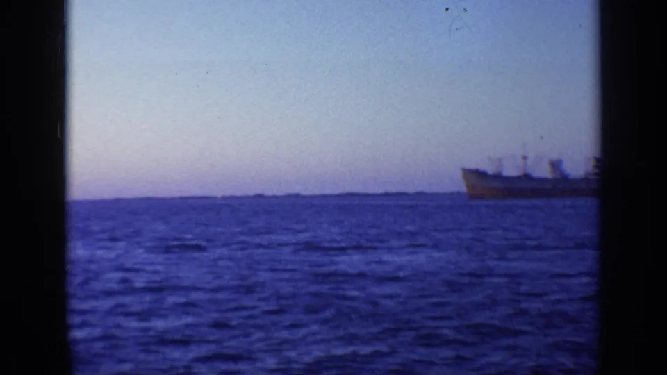 1968 Florida 8mm frame with a distant cargo ship on the right, open water in front, and a faint land horizon under a pale sky.