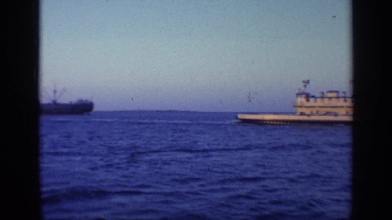 Large vessel on blue water with a distant ship at left and dark film borders.