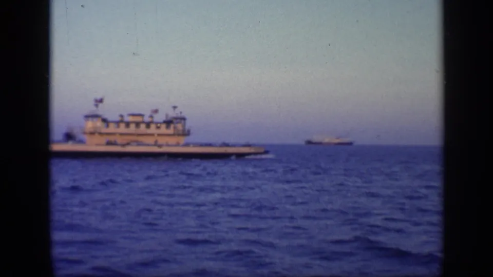 1968 Florida 8mm frame showing a white vessel moving across blue water, with a distant ship shape near the horizon.