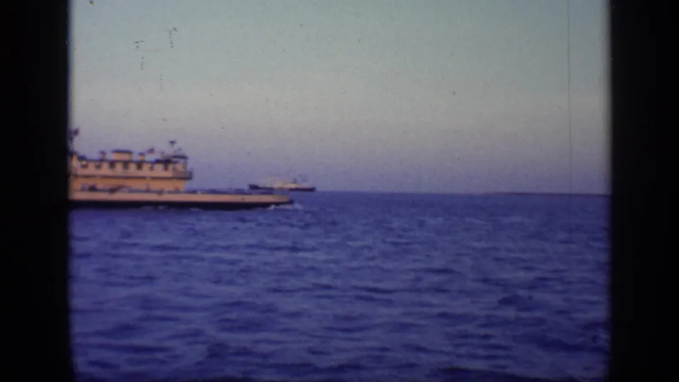 1968 Florida home-movie frame with a large white vessel partly left of center, open ocean, and a small distant ship on the horizon.