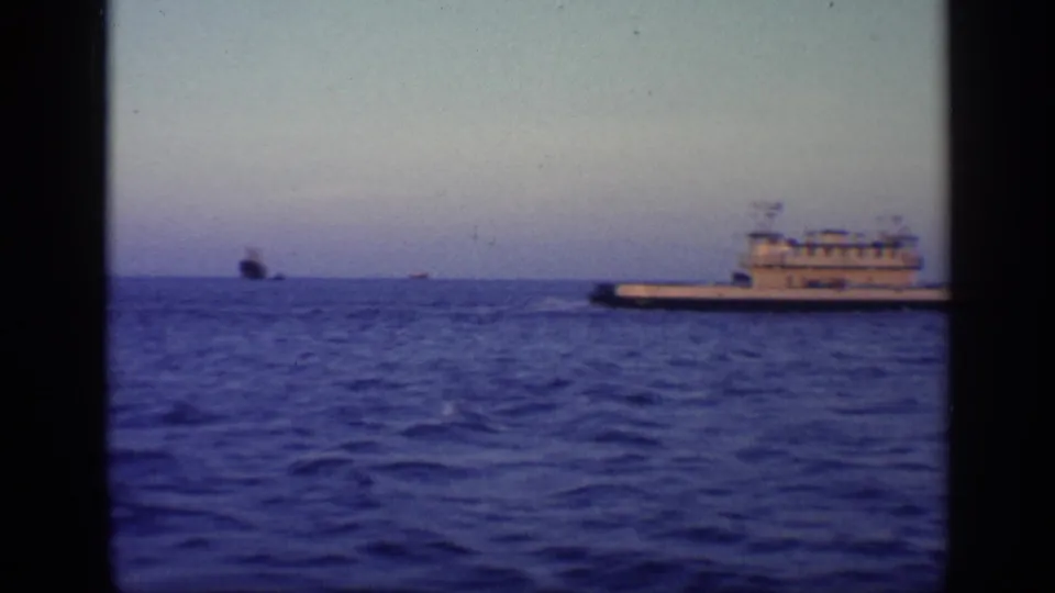 1968 Florida home-movie frame showing the vessel near the right edge, with open water and distant ship silhouettes near the horizon.