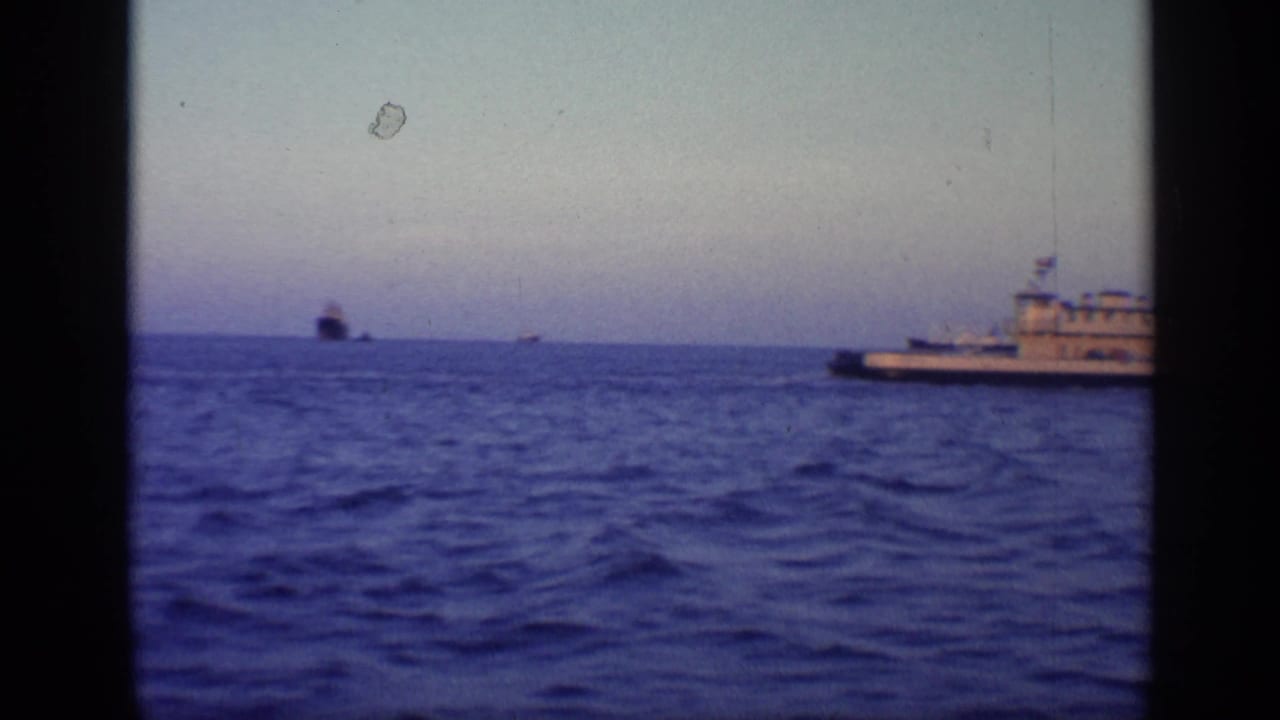 Blue ocean at dusk with distant ships and part of a vessel near the right edge.