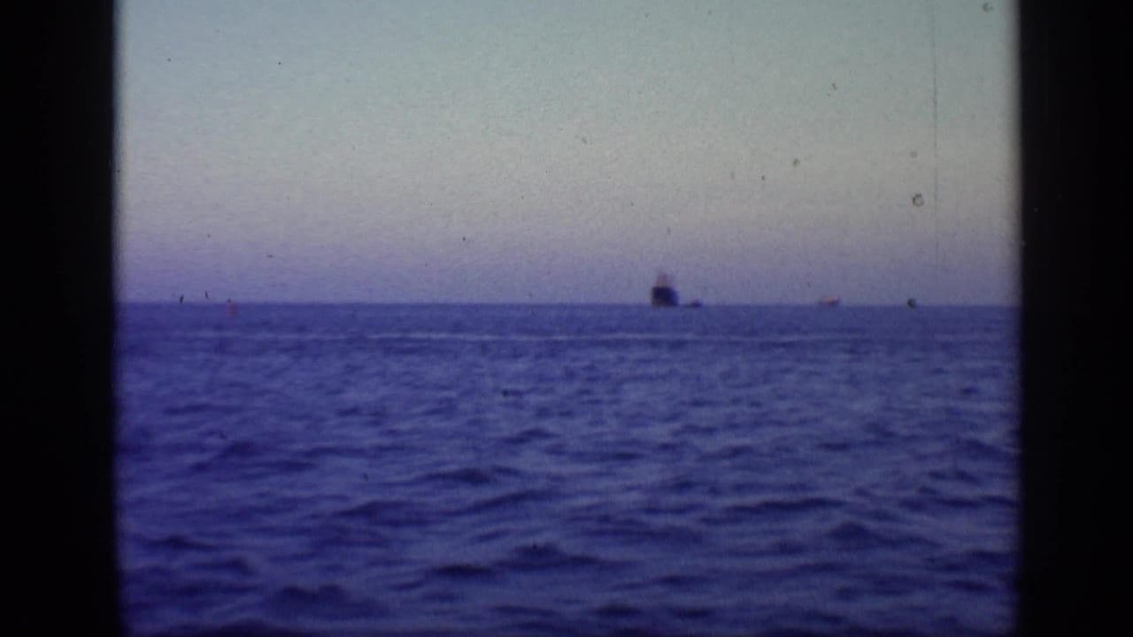 Open ocean with a low horizon and a dark ship silhouette in the distance.