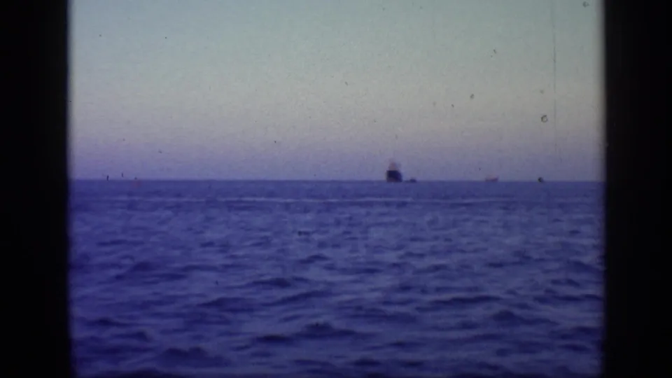1968 Florida 8mm frame of open water at twilight, with a distant dark ship on the horizon and visible film gate edges.