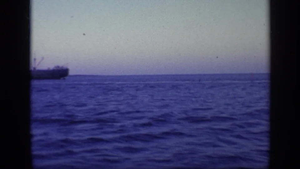 1968 Florida 8mm frame from a boat, with textured blue water and part of a large ship cropped at the left horizon.