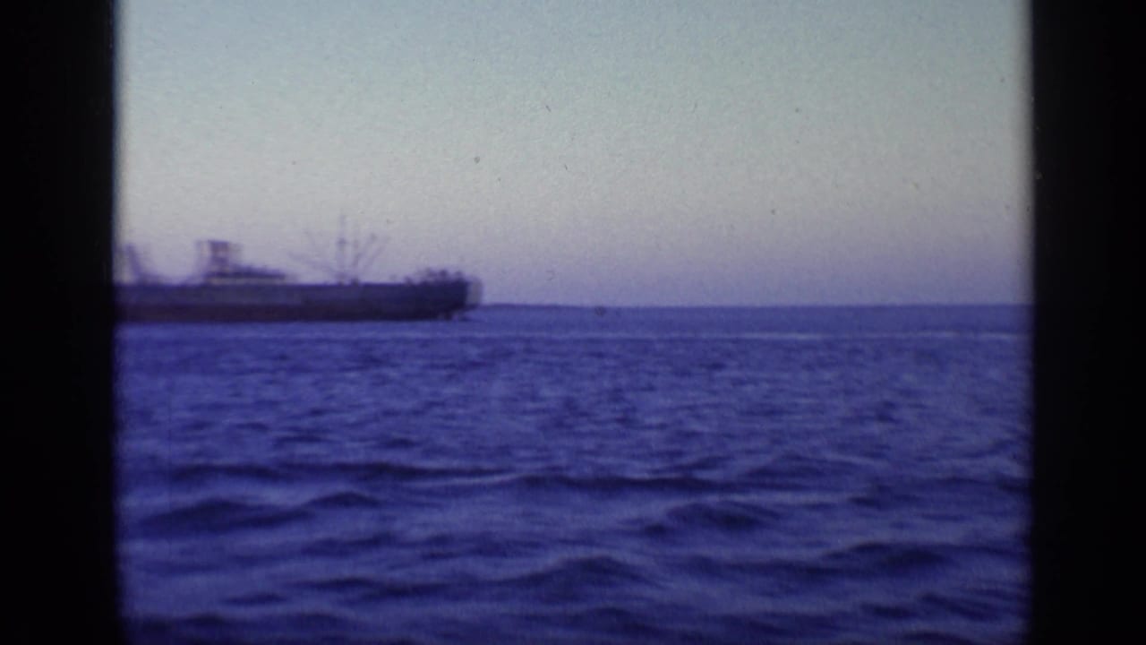 Distant cargo ship on blue water under a pale sky.
