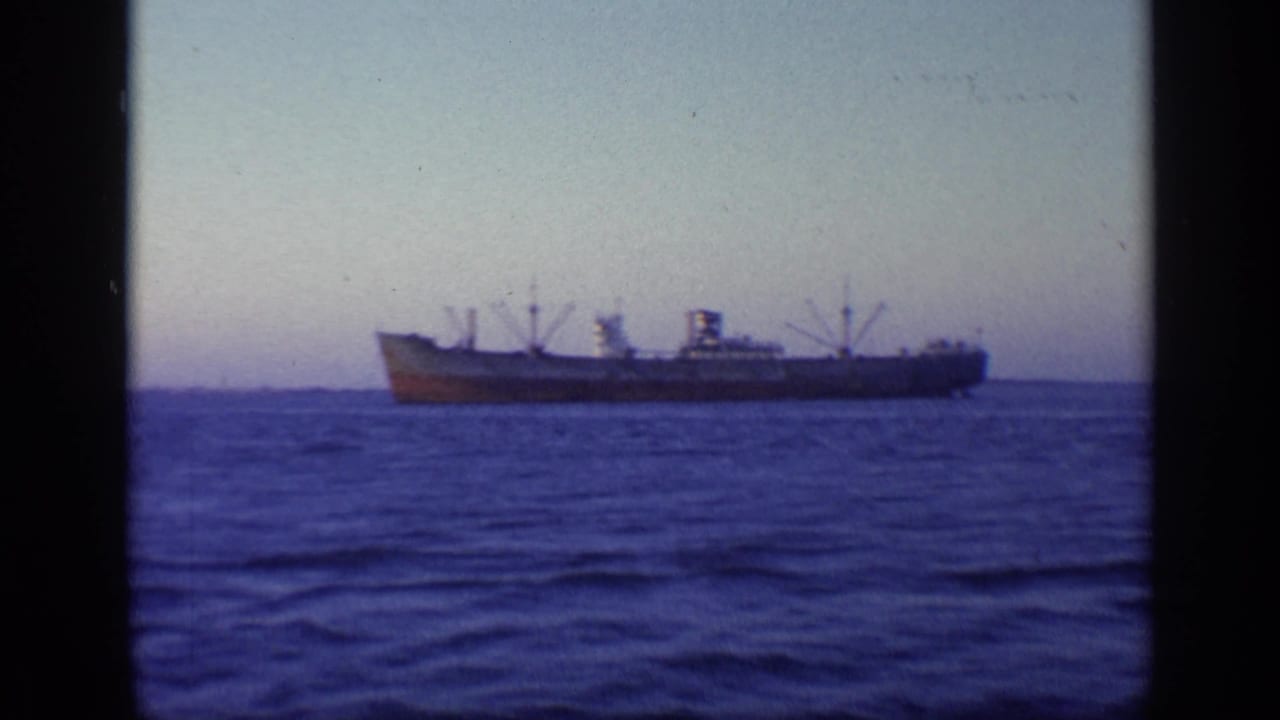 A large cargo ship appears in profile on the horizon in 1968 Florida home-movie footage, with open water filling the foreground.