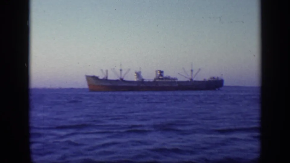 A large cargo ship appears in profile on the horizon in 1968 Florida home-movie footage, with open water filling the foreground.