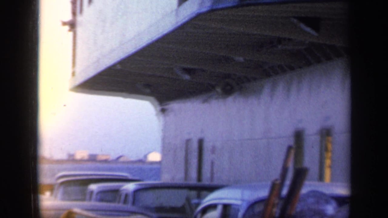 Ferry deck with several classic cars parked beneath a large ship structure.