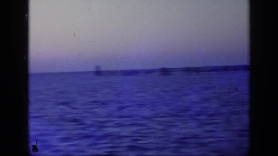 A handheld 8mm view from the ferry shows calm water and a distant linear pier or shoreline form.
