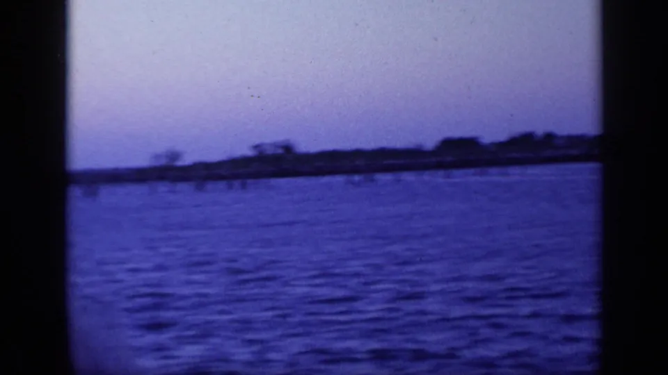The ferry approaches or passes a low Florida shoreline, seen as dark shapes across blue twilight water.