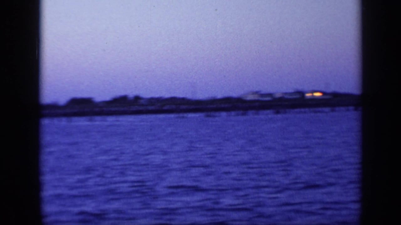Purple dusk water view with distant low shoreline and a dark vertical film-frame edge.