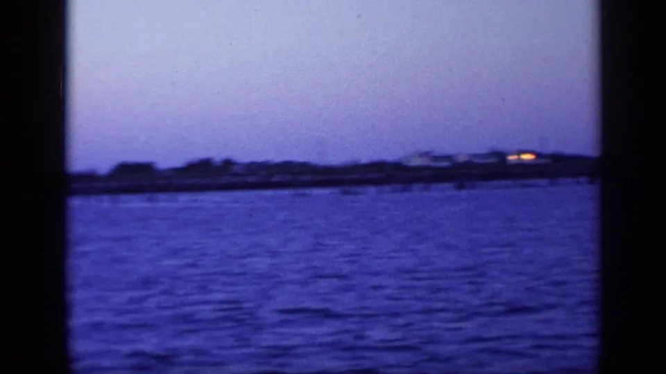 1968 Florida 8mm frame showing calm harbor water at dusk with a low shoreline under a purple-blue sky.