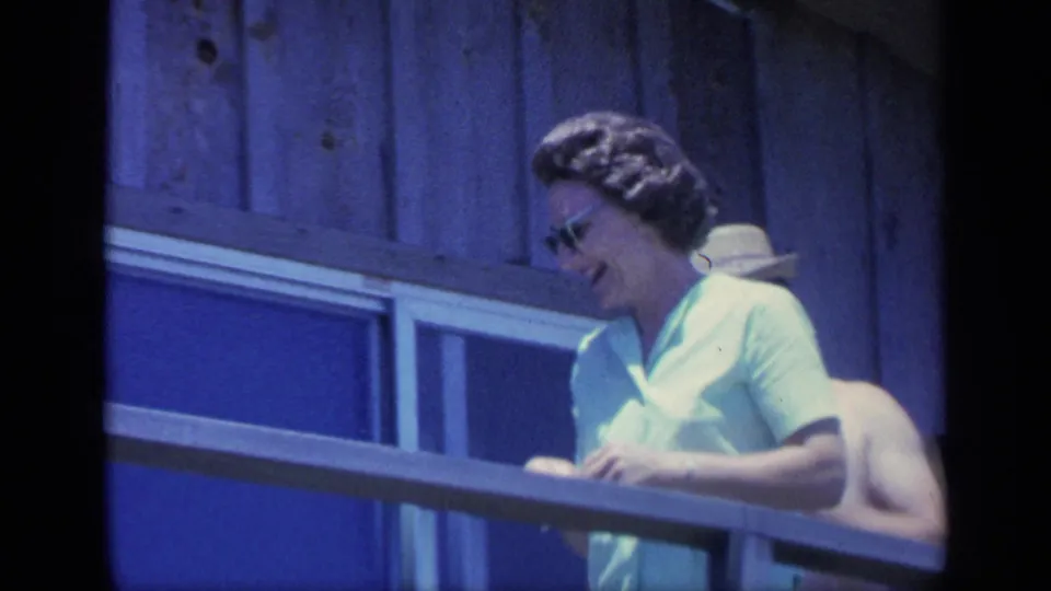1968 Florida 8mm frame showing a woman in sunglasses leaning at a sunny wooden balcony.