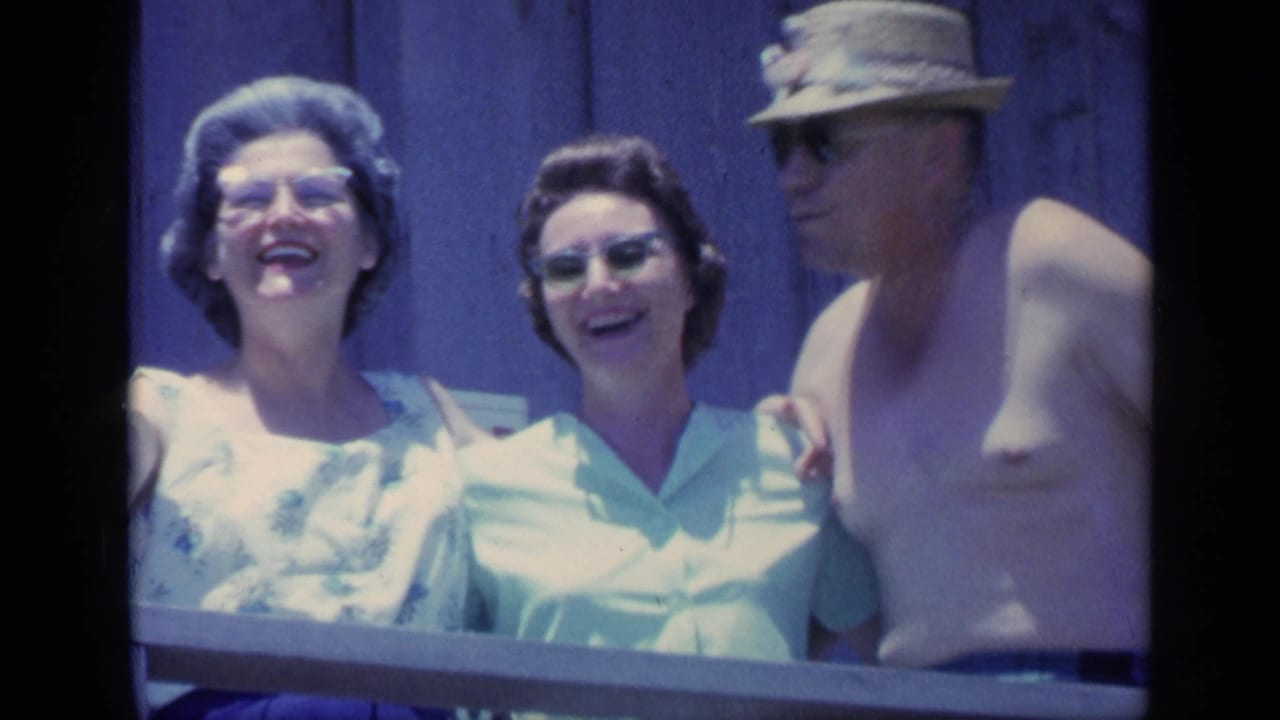 1968 Florida frame showing three adults laughing on a wooden porch, with sunglasses, straw hat, and bright daylight.