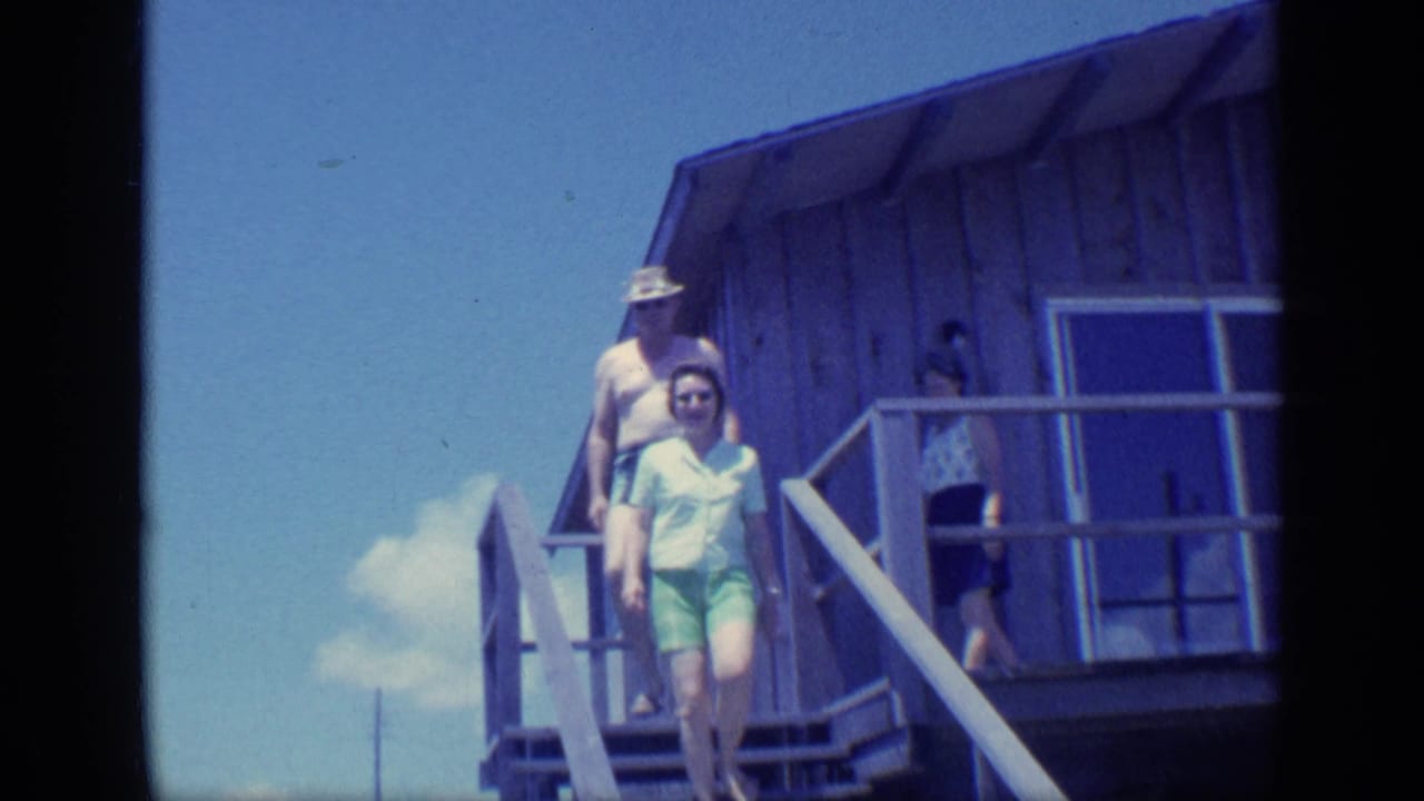 Three adults descend wooden outdoor stairs beside a cabin under a blue sky.