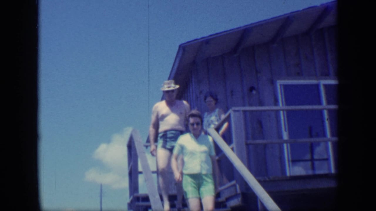 A shirtless man and woman in light green shorts descend stairs from a wooden deck.