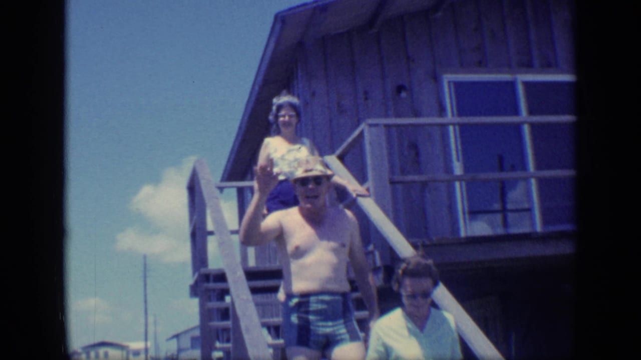 Adults descend wooden stairs outside a raised beach house under a bright sky.