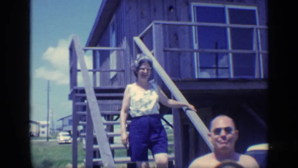 1968 Florida beach-house frame with a woman in blue shorts on the stairs and a shirtless man partly visible below.