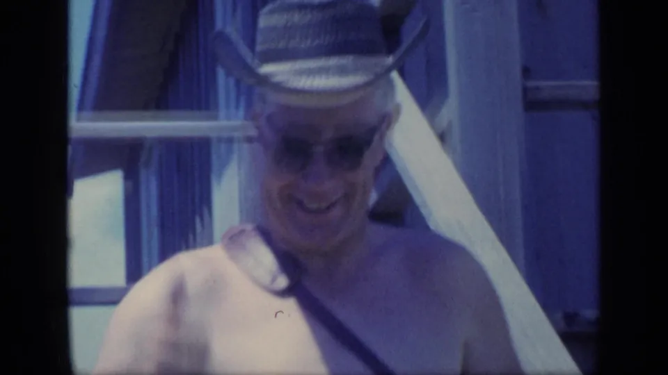 The man descends wooden stairs, still wearing sunglasses and a cowboy-style hat, in a handheld 1968 Florida vacation shot.