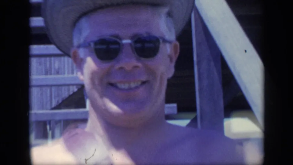 Close 8mm frame of a smiling shirtless man in sunglasses and a cowboy-style hat near wooden stairs in Florida, 1968.