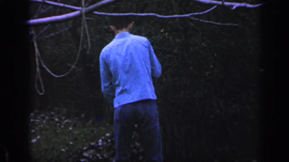 The man remains in the wooded Florida backyard, partly turned away as a rake handle appears near him under low natural light.