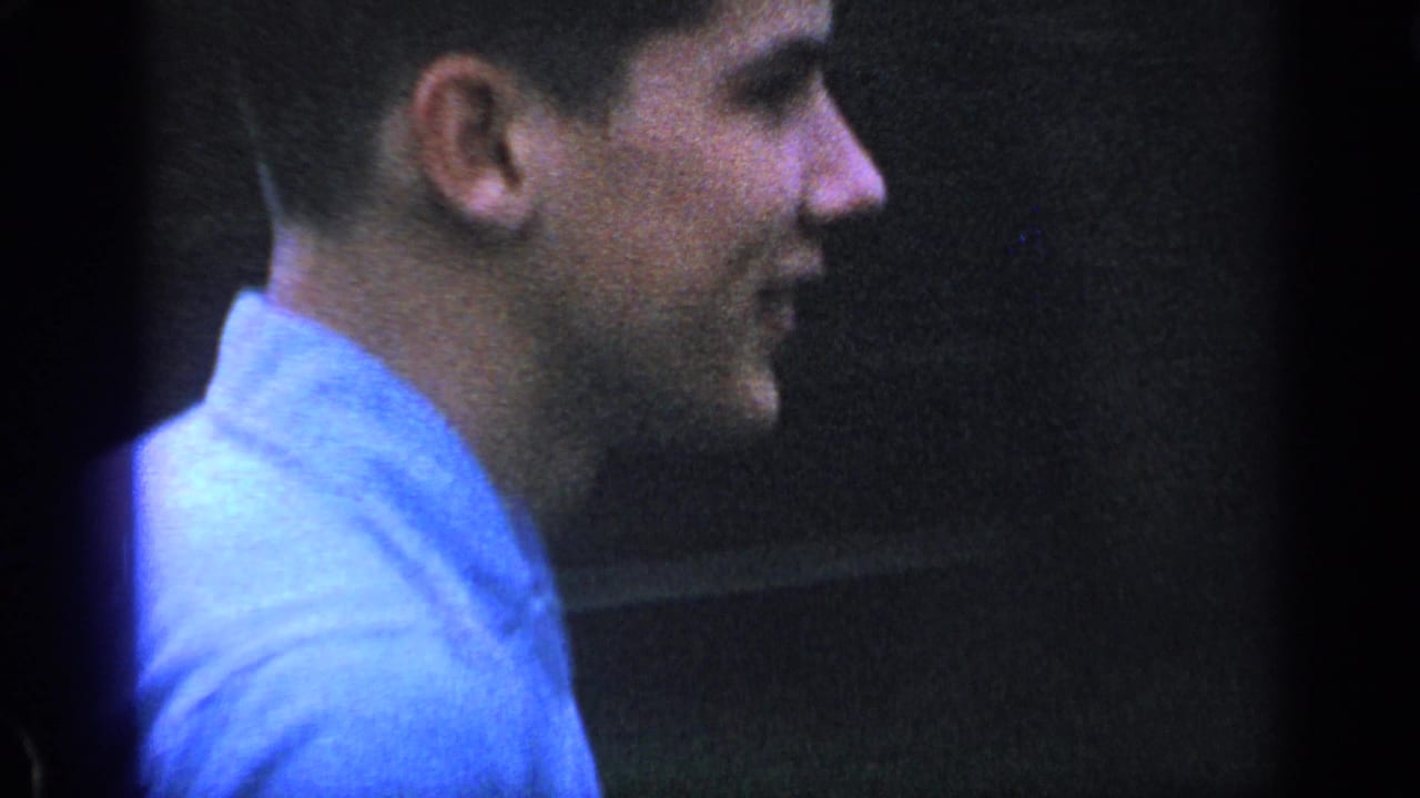Close side view of a young man in a blue shirt near a house wall.