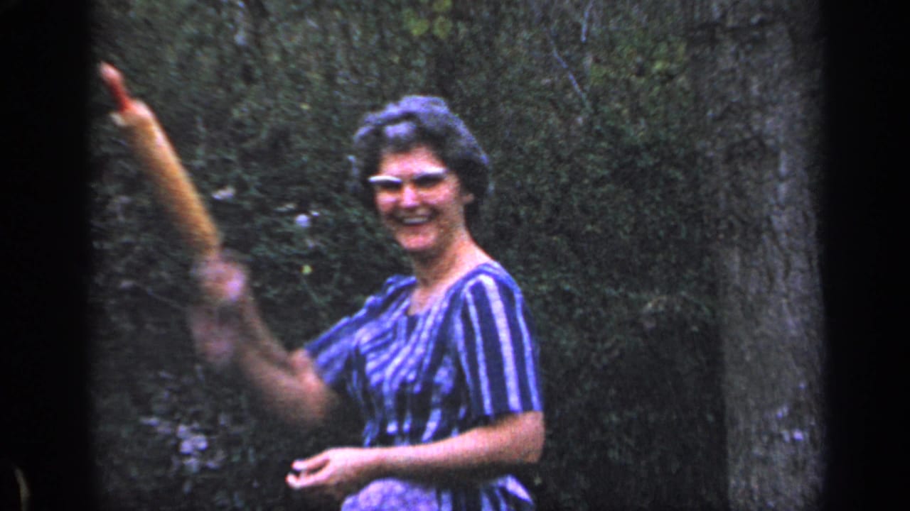 Woman in striped dress smiling and waving in a green garden.