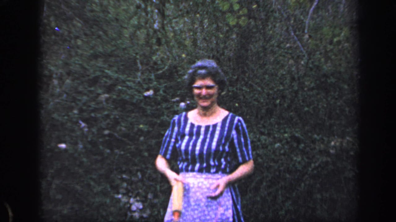 Woman in an apron smiles while holding a rolling pin at waist height.