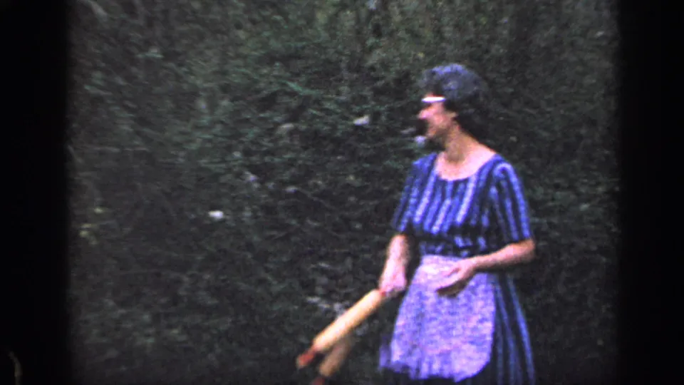 At the end of the 1968 Florida clip, the woman looks off to the side with the rolling pin lowered, standing against dense yard greenery.