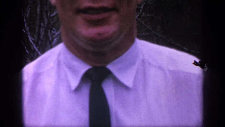A close 8mm crop shows the man's lower face, white shirt, dark tie, and shoulders with the outdoor background mostly obscured.