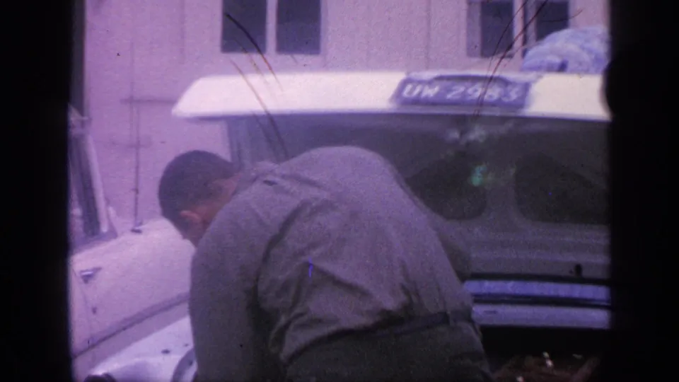 1968 Florida frame showing a man leaning into the open trunk of a white car, with the license plate and car rear in view.