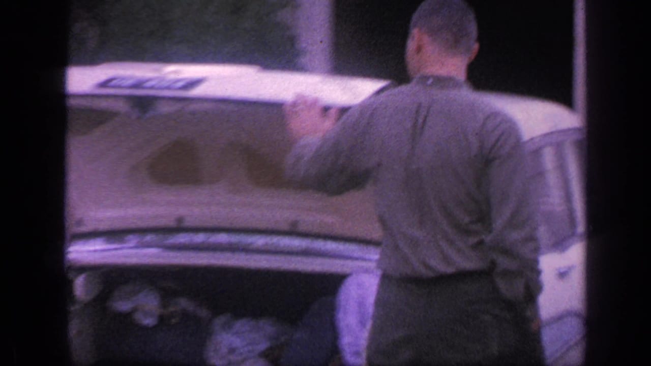 Man stands behind a white classic car with the trunk open.