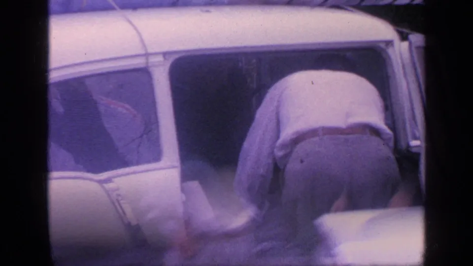 A man in a light shirt and trousers leans into the open door of the white car during the 1968 Florida family trip preparation.
