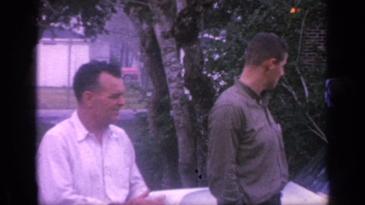 The older man in a white shirt appears to gesture while speaking, as the younger man in a green shirt looks away in a Florida yard.