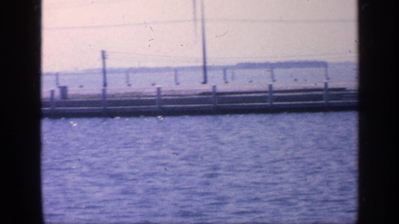 Open water seen past boat windows with a distant pier or dock and shoreline.