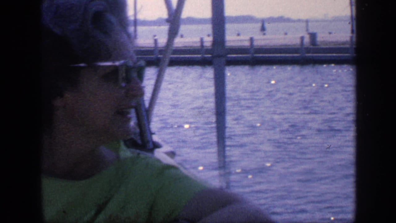 Woman in sunglasses and a green dress seated or standing on a boat near the water.