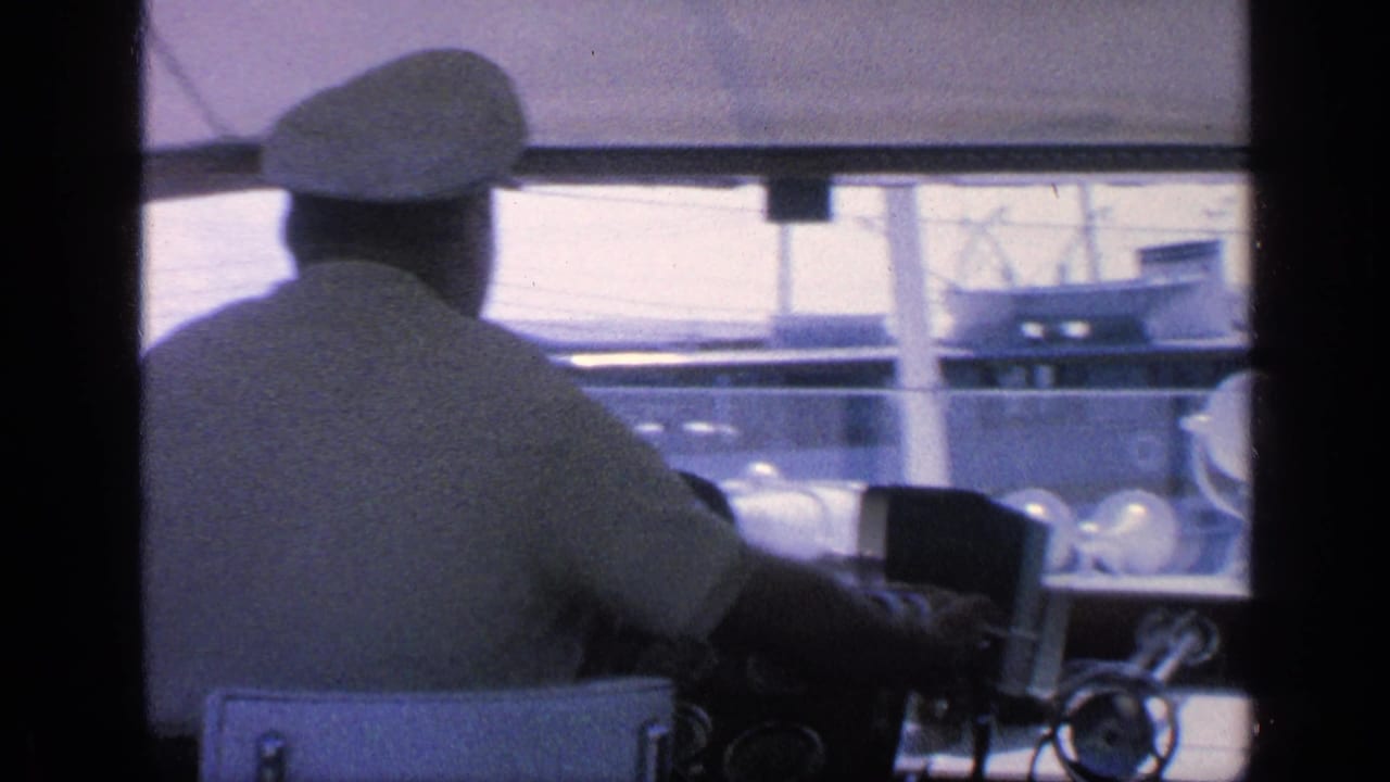 1968 Florida home-movie frame showing a captain in a white cap at the yacht helm with marina structures visible ahead.