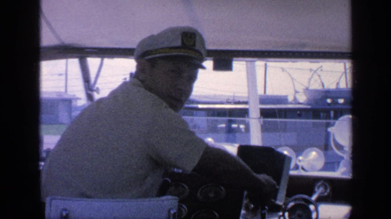 1968 Florida yacht helm view with the captain in a white cap turning toward the camera inside the cabin.