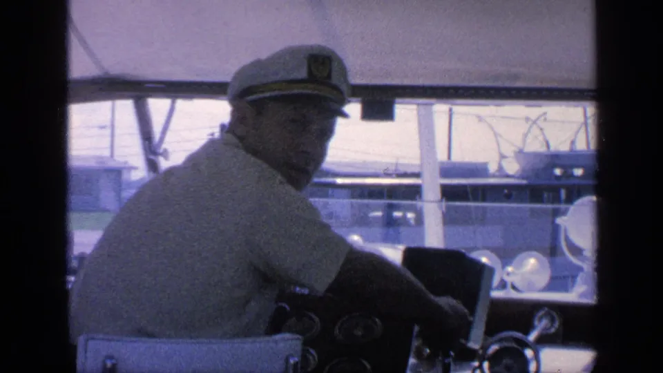 1968 Florida yacht helm view with the captain in a white cap turning toward the camera inside the cabin.