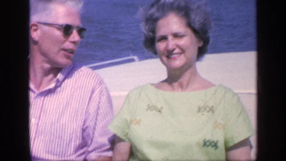 A smiling woman sits beside a man in sunglasses on a boat, with calm Florida water in the background.