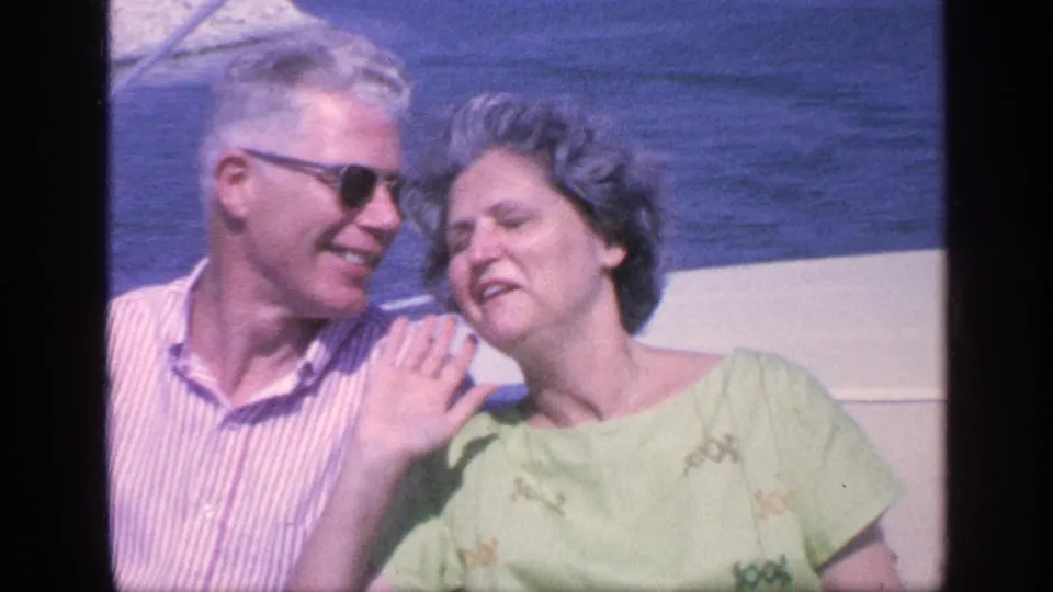 An older couple on a boat in Florida, the man in sunglasses and striped shirt as the woman leans near him against blue water.